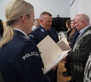 Policjantka, a a nią komendant, który wręcza dyplom pracownikowi cywilnemu.