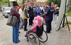 Grupa uczestników gry miejskiej wykonujących zadanie związane z przeniesieniem maskotki za pomocą wózka.
