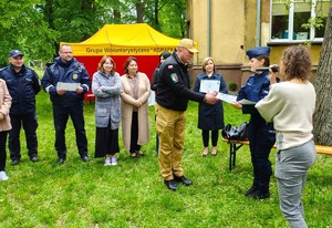 Komendant Komendy Powiatowej Państwowej Straży Pożarnej w Pabianicach otrzymuje podziękowanie od policjantki, w tle pozostałe osoby.