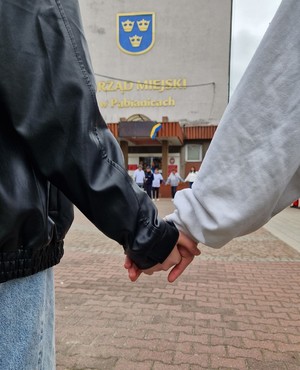 Splecione ręce na tle budynku Urzędu Miasta w Pabianicach.