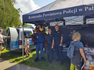 Policjanci i maskotka pod policyjnym namiotem.