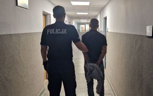 Umundurowany policjant stoi z zatrzymanym mężczyzną.