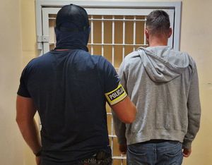 Nieumundurowany policjant stoi z zatrzymanym mężczyzną.
