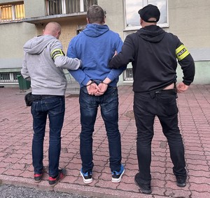 Policjanci prowadzą do komendy poszukiwanego listem gończym mężczyznę.