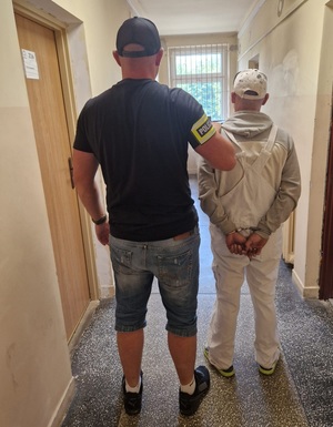 Nieumundurowany policjant prowadzi zatrzymanego mężczyznę.