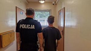 Umundurowany policjant stoi z zatrzymanym mężczyzną.