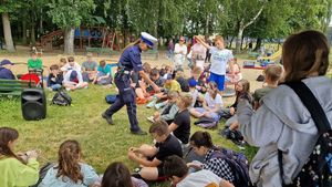 Policjantka podaje mikrofon chłopcu by udzielił odpowiedzi na zadane przez nią pytanie, reszta uczestników wydarzenia przygląda się sytuacji.
