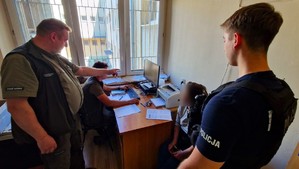 Policjant i strażnicy leśni wykonujący czynności z zatrzymaną kobietą.
