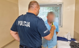 Policjant bada zatrzymanego mężczyznę alkomatem.