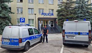 Policjant stojący pomiędzy oznakowanymi radiowozami. W tle Komenda Powiatowa Policji w Pabianicach.