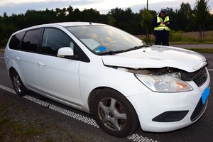 Policjant wykonujący czynności przy białym samochodzie osobowym uczestniczącym w zdarzeniu.