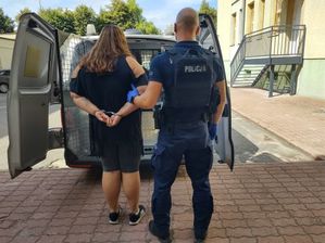 Umundurowany policjant stoi z kobietą tyłem do zdjęcia. W tle policyjny radiowóz.