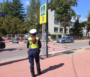 Umundurowana policjantka stoi przed znakiem przejście dla pieszych. W tle szkoła.