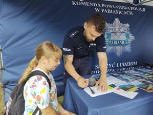 Policjant wraz z dziewczynką stoją przy stole pod namiotem.