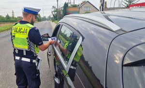 Policjant wręcza kierującemu materiały informacyjne dotyczące kampanii Mistrzu, zwolnij.