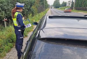 Policjantka wręcza kierującemu materiały informacyjne dotyczące kampanii Mistrzu, zwolnij.