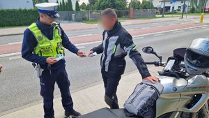 Policjant wręcza motocykliście materiały informacyjne dotyczące kampanii Mistrzu, zwolnij.