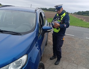 Policjant kontroluje kierującego w niebieskim aucie.