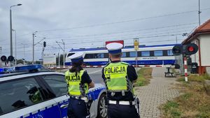 Policjanci stoją przed zamkniętym przejazdem kolejowym.