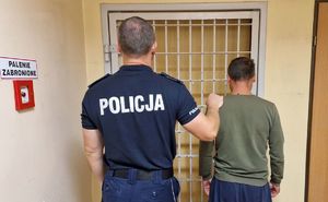 Umundurowany policjant stoi z zatrzymanym mężczyzną.