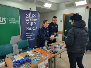 Policjanci stoją przy stoisku profilaktycznym przy którym znajduje się również zainteresowana inicjatywą kobieta.