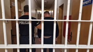 Policjant stoi z zatrzymanym mężczyzną, obaj znajdują się za kratami.
