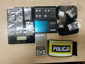 Zabezpieczone substancje odurzające, wagi i policyjna opaska naramienna.