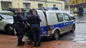 Policjanci doprowadzają zatrzymanego do radiowozu.