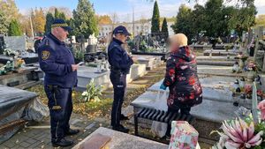 Policjantka i strażnik miejski na cmentarzu rozmawiają z kobietą porządkującą groby.