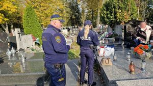 Policjantka i strażnik miejski na cmentarzu rozmawiają z osobami porządkującymi groby.