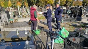 Policjantka i strażnik miejski na cmentarzu rozmawiają z kobietą porządkującą groby.
