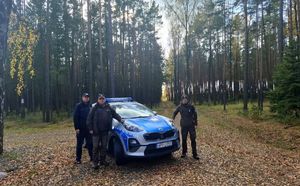 Leśnicy i dzielnicowi stoją przy radiowozie na terenie lasu.
