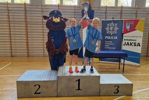 Zwycięska drużyna stoi na podium. Dzieci mają w rękach puchar. Obok nich znajduje się maskotka pabianickich policjantów.