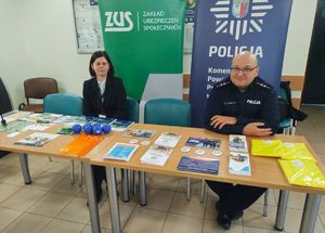 Policjant i pracownica Zakładu Ubezpieczeń Społecznych przy stoisku informacyjnym.