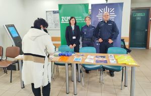 Policjant, policjantka i pracownica Zakładu Ubezpieczeń Społecznych przy stoisku informacyjnym.