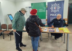 Policjant wręcza materiały informacyjne seniorom.