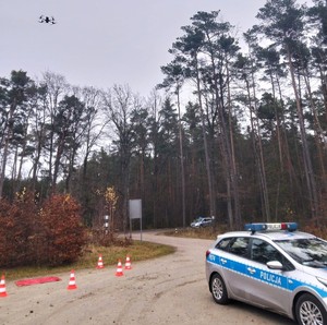 Teren leśny. Policyjne radiowozy nad nimi dron.