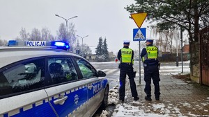 Policjanci stoją przed radiowozem przy przejściu dla pieszych.