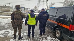 Policjant, funkcjonariusz Służby Ochrony Kolei i żołnierz stoją na dworcu obok pojazdu Służby Ochrony Kolei.