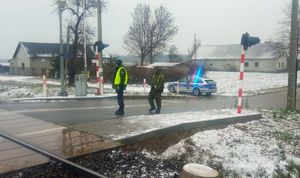 Funkcjonariusz Służby Ochrony Kolei i żołnierz stoją na przejeździe kolejowym, w tle widać radiowóz.