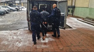 Policjanci stoją z zatrzymaną kobietą przed radiowozem.