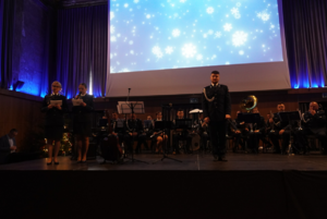 Policjanci grający na instrumentach. Z przodu widać policjantki i dyrygenta stojących na scenie.