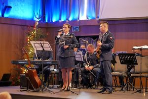 Policjanci grający na instrumentach. Policjantka śpiewa do mikrofonu.