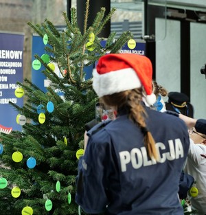 Policjantka w czapce Świętego Mikołaja stoi przy odblaskowej choince.