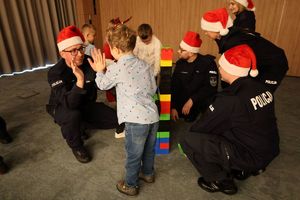 Policjanci w czapkach Świętego Mikołaja bawią się z dziećmi.