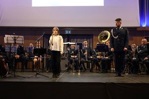 Dziewczynka stoi na tle orkiestry i mówi wierszyk.