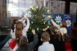 Dzieci ubierają odblaskową choinkę.
