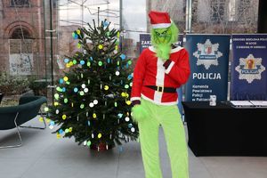 Przed ubraną odblaskową choinką stoi Grinch.