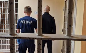 Policjant stoi z zatrzymanym mężczyzną na tle krat.