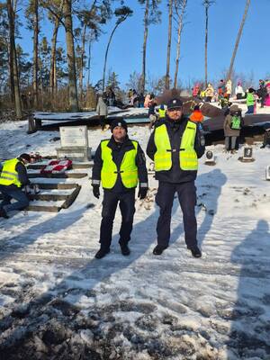 Dwóch policjantów ma tle lasu, w którym są dzieci.